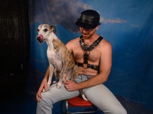 Blake is shirtless except for a leather harness. His dog, Fuji, sits on his lap.